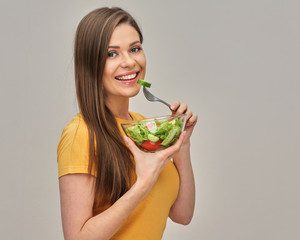 girl wearing yellow T-shirt eating salad with lettuche from glass bowl. isolated studio portrait.