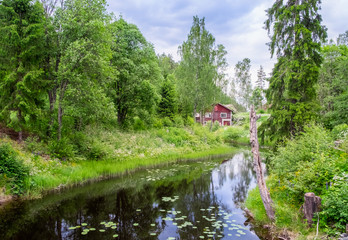 Idyllic river with old abandoned cottage and green lush trees at summer day in Finland
