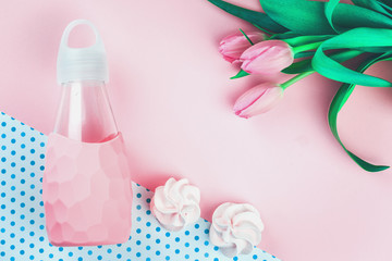 Tender tulip flowers and pink trendy feminine glass water bottle with two cookies on a dotted background, flat lay with copy space for blogger