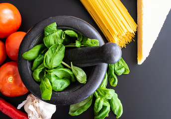 preparing italian pasta with fresh basil in mortar, tomatoes, garlic, pepper and Parmesan on dark kitchen counter