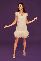 Naklejka premium Beautiful brunette woman in elegant cocktail white dress is posing in studio on purple background.