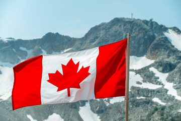 Beautiful Canadian Flag waving for the strong wind, tall mountains in the background