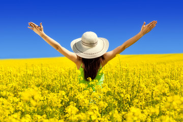 Fototapeta na wymiar rear view of young woman with hat, arms raised, Canola field blossom