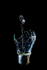 Creative broken light bulb with art water fountain on isolated black background with flash. The concept of absurd imagination and implementation of non-standard thinking. Isolated black background.