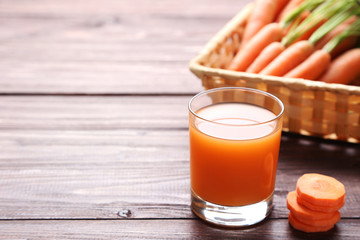 Fresh carrot with glass of juice on wooden table