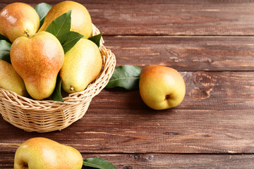 Ripe pears and green leafs in basket on brown wooden table