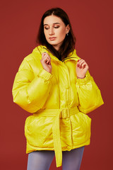 Studio portrait of young brunette woman in yellow down jacket and grey blue panty hoses or...