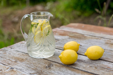Jar with lemon water and lemons on wooden table, standing outside. Summer time.