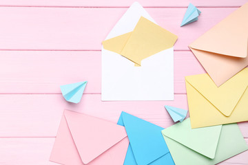 Colorful envelopes with paper planes on pink wooden table
