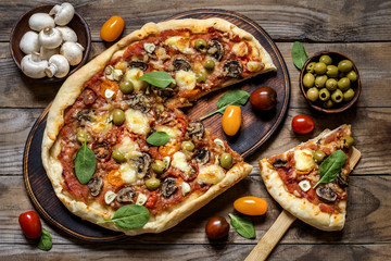 pizza with mushrooms, tomatoes, olives and spinach and goat cheese on wooden background