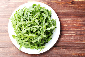 Green arugula leafs in plate on brown wooden table