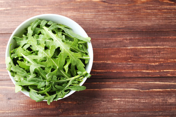 Green arugula leafs in bowl on brown wooden table