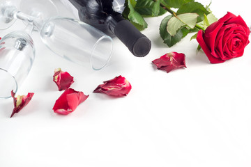 Bottle of wine, glass and red rose with petals on a white background
