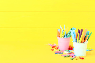 Colorful plastic clothespins in buckets on yellow background