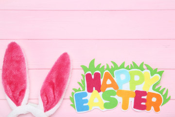 Rabbit ears with text Happy Easter on pink wooden table