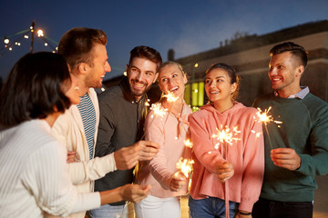 leisure, celebration and people concept - happy friends with sparklers at rooftop party at night