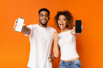 Cheerful black couple showing blank smartphones at camera