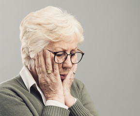 Sad lonely elderly woman posing with head in hands