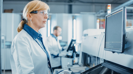 Portrait Shot of a Female Engineer On High Tech Factory Uses Computer for Programing Pick and Place Electronic Machinery for Printed Circuit Board Surface Mount Assembly Line.