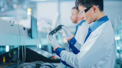 High-Tech Factory: Quality Control Engineer Picks up and Visually Checks Smart Electronic Device...