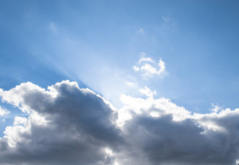 Obraz premium Sunbeam, white and dark cumulus clouds in the blue sky.