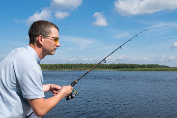 side view, a man with glasses is fishing for spinning in open water