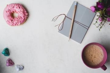 Flat lay with marble background and pink flowers with coffee mug and donut lace and notepad 
