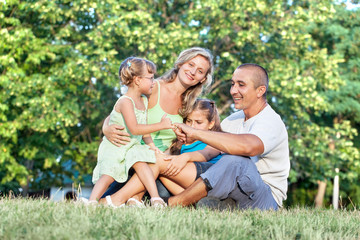Fototapeta premium Happy family with two daughters sitting on the grass in park