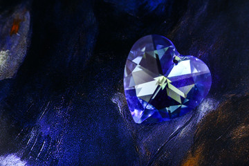 Sparkling heart-shaped blue crystal similar to diamond on the dark color background. 