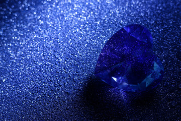 Sparkling heart-shaped blue crystal similar to diamond on the dark color background. 