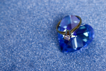 Golden engagement ring with gem of diamond fixed on the blue heart-shaped crystal.