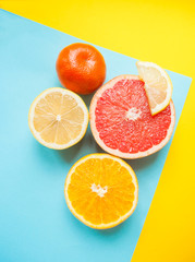 Flat lay of cut ripe juicy grapefruit, lemon and orange on yellow and blue background. Citrus pattern.