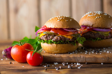 Classic american cheeseburger on a wooden board with tomatoes and onion.