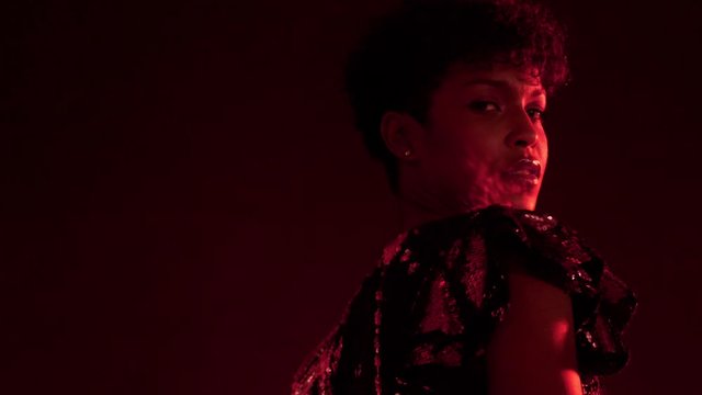 closeup portrait of mixed race african american woman with short hair in night club in red light turning to the camera and light reflect to her cheek from sparkly dress