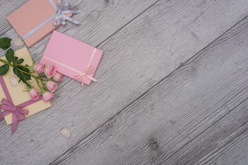 Hands holding craft paper pink gift boxes with as a present for Christmas, new year, valentine day, mothers day and womans day or anniversary on wooden background decorated with roses.
