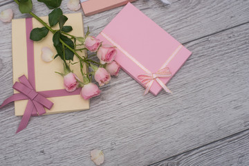 Hands holding craft paper pink gift boxes with as a present for Christmas, new year, valentine day, mothers day and womans day or anniversary on wooden background decorated with roses.