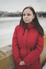 Beautiful girl in a red jacket on the pier in the spring posing against the water. Woman on the waterfront