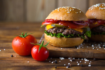 Classic american cheeseburger on a wooden board with tomatoes and onion.