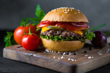 Classic american cheeseburger on a wooden board with tomatoes and onion.