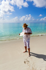 Mature man holding old damaged paper on a tropical beach 