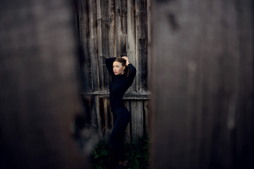 beautiful woman with brunette hair in black clothes posing on dark wooden fence background