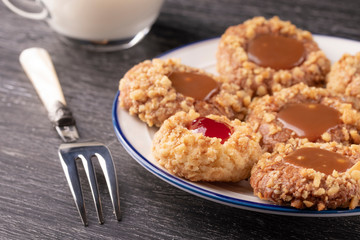 Shortbread cookies made of walnut dough with strawberry jam and caramel on a plate with a fork. Glass of milk.