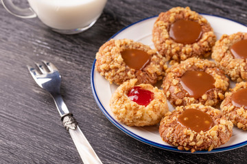 Shortbread cookies made of walnut dough with strawberry jam and caramel on a plate with a fork. Glass of milk.