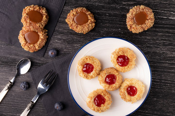 Shortbread cookies made of walnut dough with strawberry jam and caramel on a plate with blueberries.
