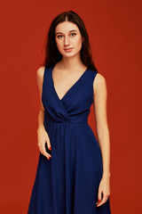 Beautiful young brunette woman in elegant blue cocktail dress with deep decollete is posing for the...