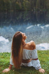 Young beautiful woman sitting on the grass next to the lake