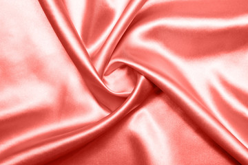 Fototapeta premium Close up of ripples on silk fabric. Satin textile background. Living Coral color. Top view. Color of the year 2019.