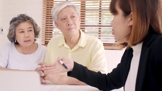 Asia smart female agent offers health insurance for elderly couples by document, tablet and laptop. Aged Asian couple consulting with insurance agent while sitting together with at home.