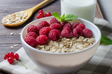 Healthy vegetarian food. Oatmeal with raspberry. Wooden spoon with cereals, milk in a glass, red currant. Brown wooden background.