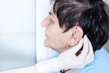 Female doctor putting a hearing aid in to the senior woman's ear 